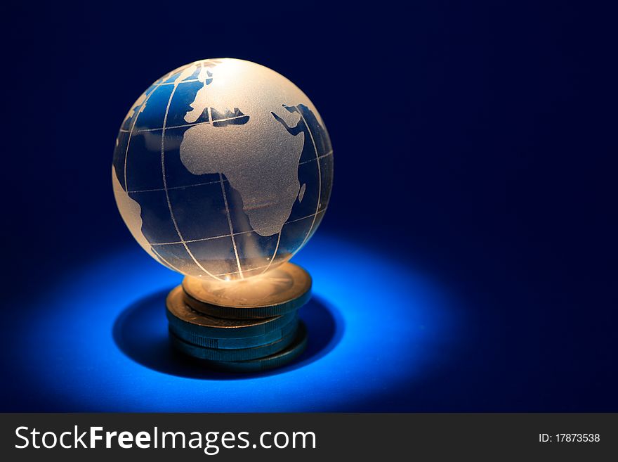 Glass globe lying on stack of coins on dark blue background with lighting effect. Glass globe lying on stack of coins on dark blue background with lighting effect