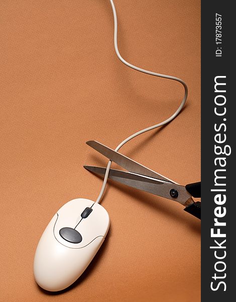 Scissors cutting cable of computer mouse on brown background. Scissors cutting cable of computer mouse on brown background