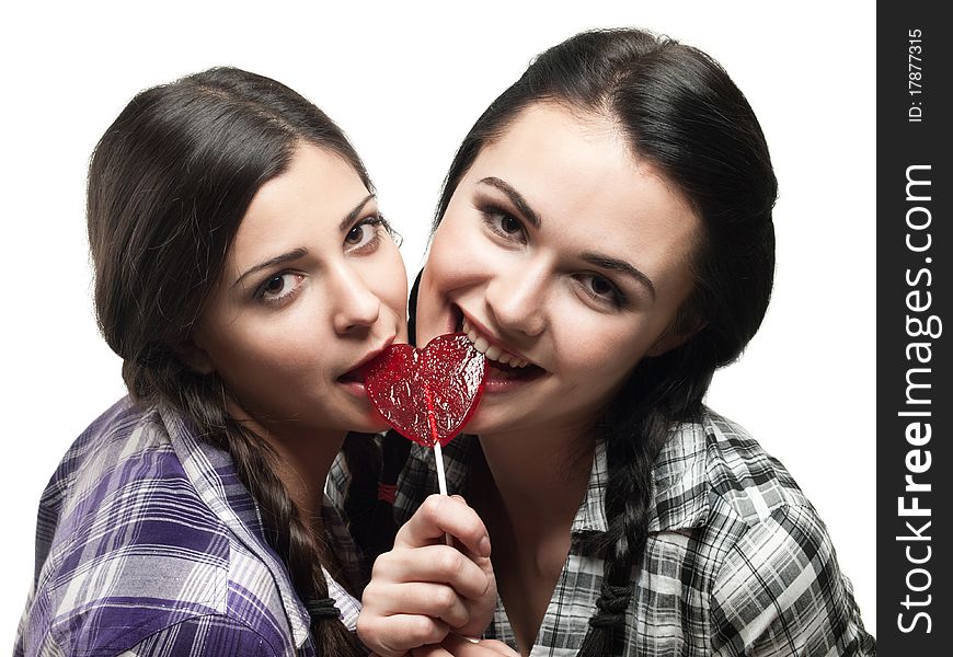 Two young smiling girl with red heart lolipop isolated on white