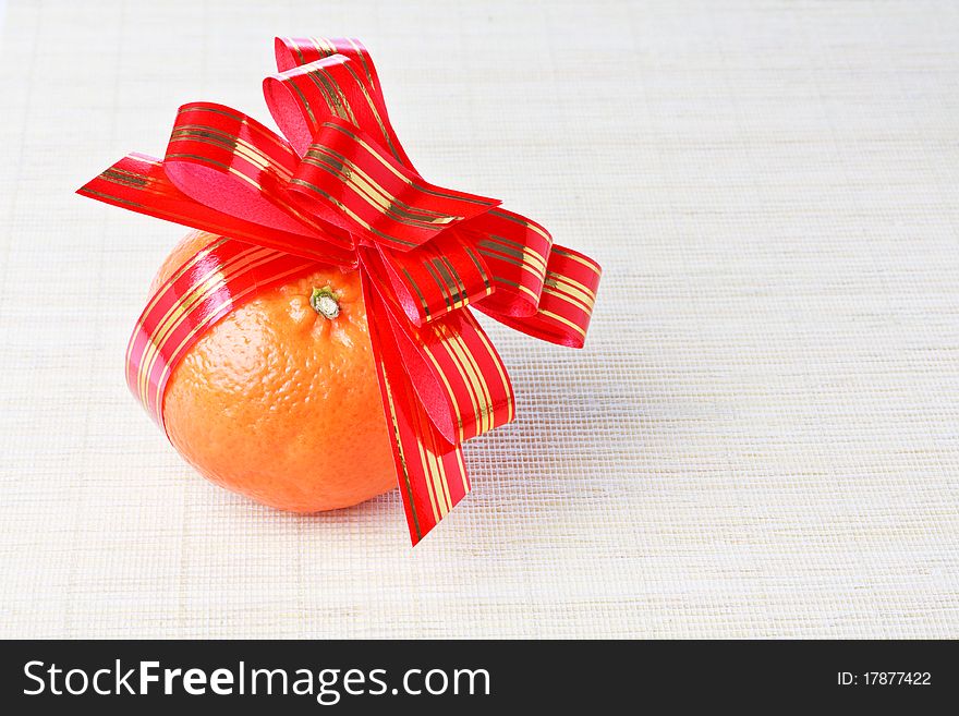 Ripe fresh orange tangerine with red goldish striped bow as a gift
