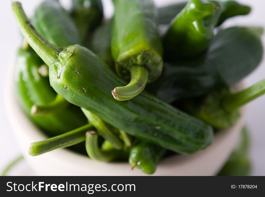 Close-up of green Spanish padron peppers in a white bowl, light background