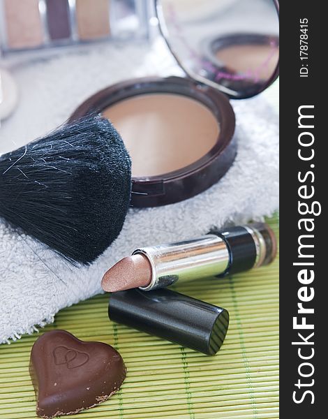 Various cosmetics and a heart-shaped chocolate resting on a bath-cloth. Various cosmetics and a heart-shaped chocolate resting on a bath-cloth