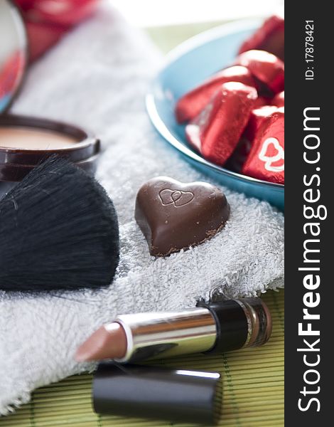 Various cosmetics and a heart-shaped chocolate resting on a bath-cloth. Various cosmetics and a heart-shaped chocolate resting on a bath-cloth