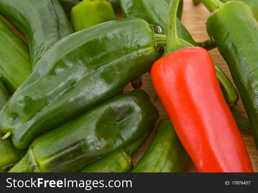 Close-up of green Spanish padron peppers and one red chilli pepper, wooden board background