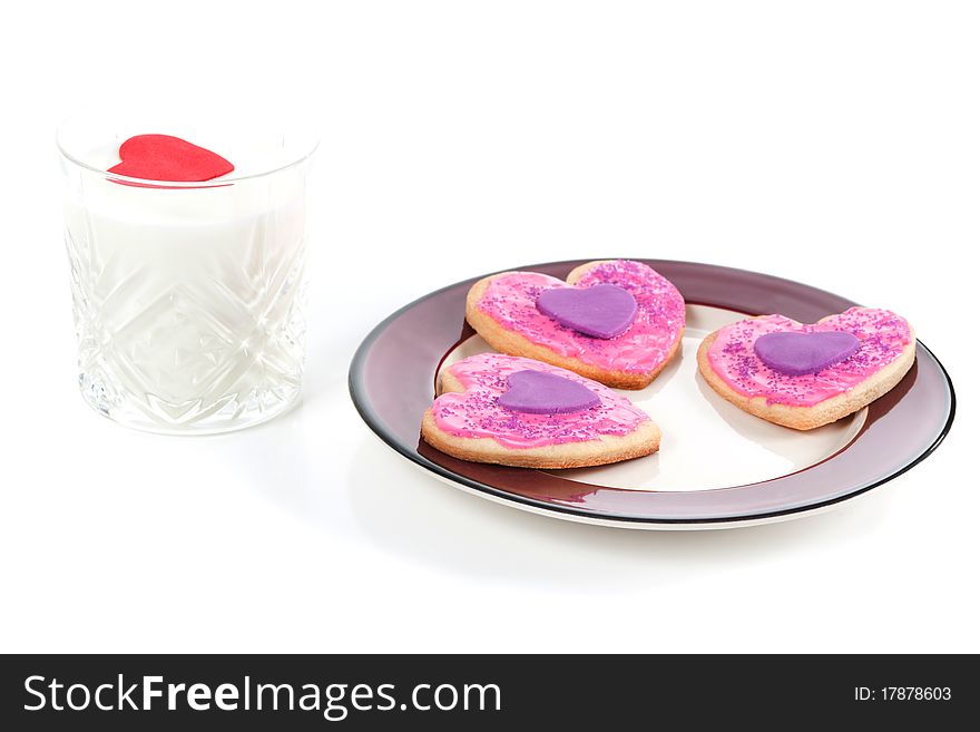 An angled closeup of a plate of homemade valentine cookies and a glass of milk with a valentine heart floating on top on a white background. An angled closeup of a plate of homemade valentine cookies and a glass of milk with a valentine heart floating on top on a white background.