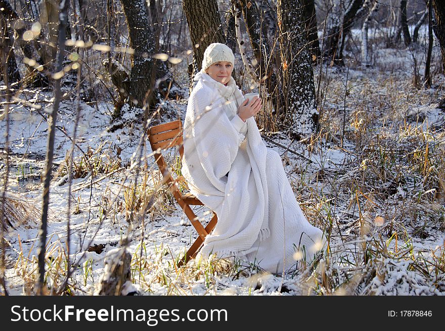 Woman in white, with a mug in his hands, wrapped in a blanket in a winter forest. sunset. Woman in white, with a mug in his hands, wrapped in a blanket in a winter forest. sunset.