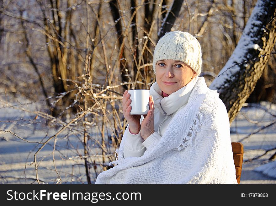 Woman in white, with a mug in his hands, wrapped in a blanket in a winter forest. Woman in white, with a mug in his hands, wrapped in a blanket in a winter forest.