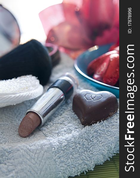 Various cosmetics and a heart-shaped chocolate resting on a bath-cloth. Various cosmetics and a heart-shaped chocolate resting on a bath-cloth