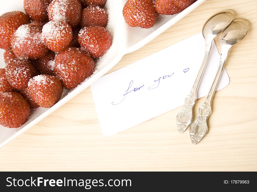 A plate of strawberries is on a wooden table. Nearby is a card with text for you. A plate of strawberries is on a wooden table. Nearby is a card with text for you