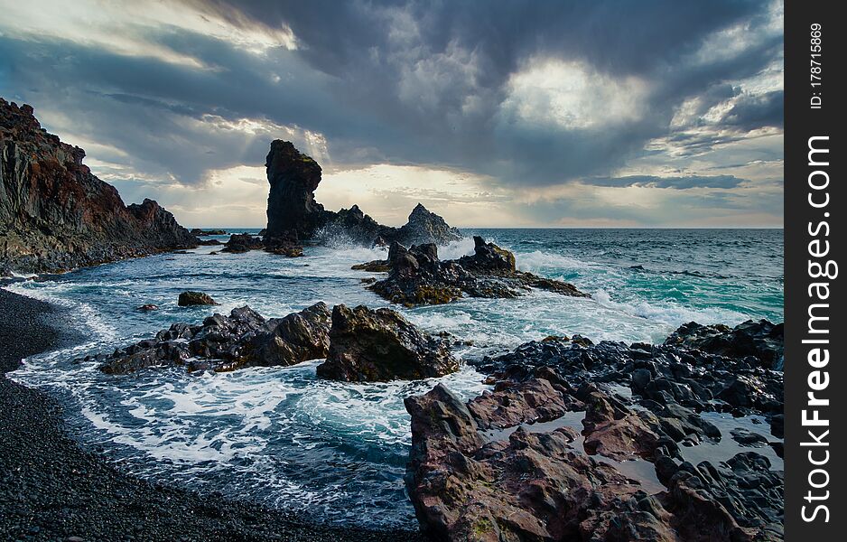 Dramatic shot of stormy coastline with black rocks and high waves on Snaefellsnes peninsula Iceland. Black clouds on sky, turquoise water. No people visible