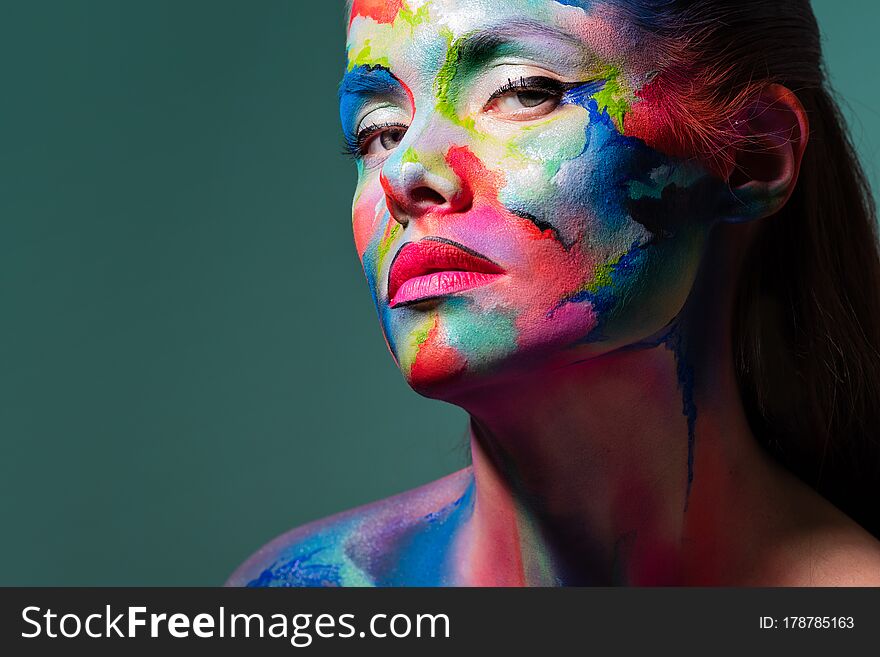 Fashion and creative makeup, young beautiful woman abstract face art, portrait on a turquoise background.
