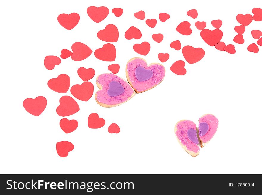 An angled view of a couple of homemade valentine cookies and a broken valentine cookie within a sea of valentines on an isolated white background. An angled view of a couple of homemade valentine cookies and a broken valentine cookie within a sea of valentines on an isolated white background.
