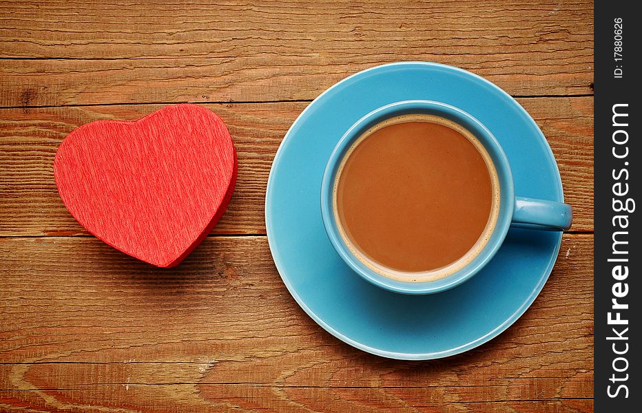 Cup of coffee and red box in heart shape on wood background