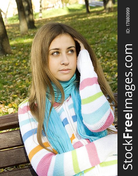 Portrait of a beautiful young woman sitting on a bench in the park around a lot of yellow, red green leaves. Portrait of a beautiful young woman sitting on a bench in the park around a lot of yellow, red green leaves