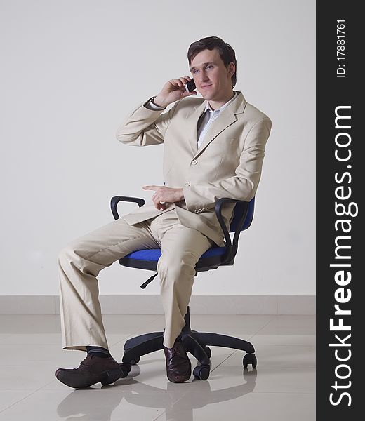 A young man in the office sitting on a chair and talking on the phone. A young man in the office sitting on a chair and talking on the phone