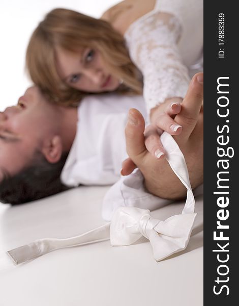 Romantic image of just married couple lying on the floor together. The groom holding a bow-tie (Focus on the bow-tie)