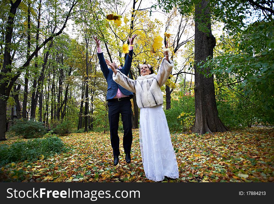 Joyful bride and groom throw the yellow leaves