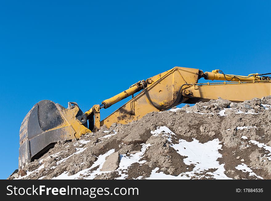 The arm and bucket of a hydraulic excavator on top of a pile of earth in winter. The arm and bucket of a hydraulic excavator on top of a pile of earth in winter.