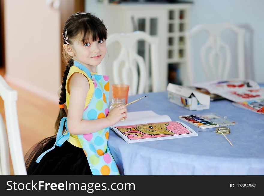 Adorable little girl with long dark hair draws in the kitchen