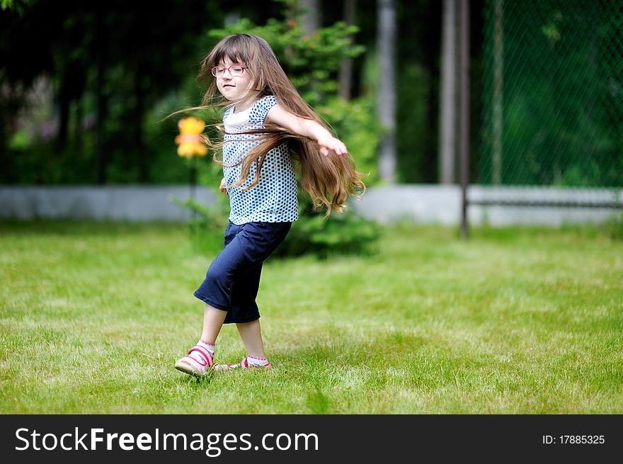 Adorable active little girl with long dark hair plays on backyard in spring