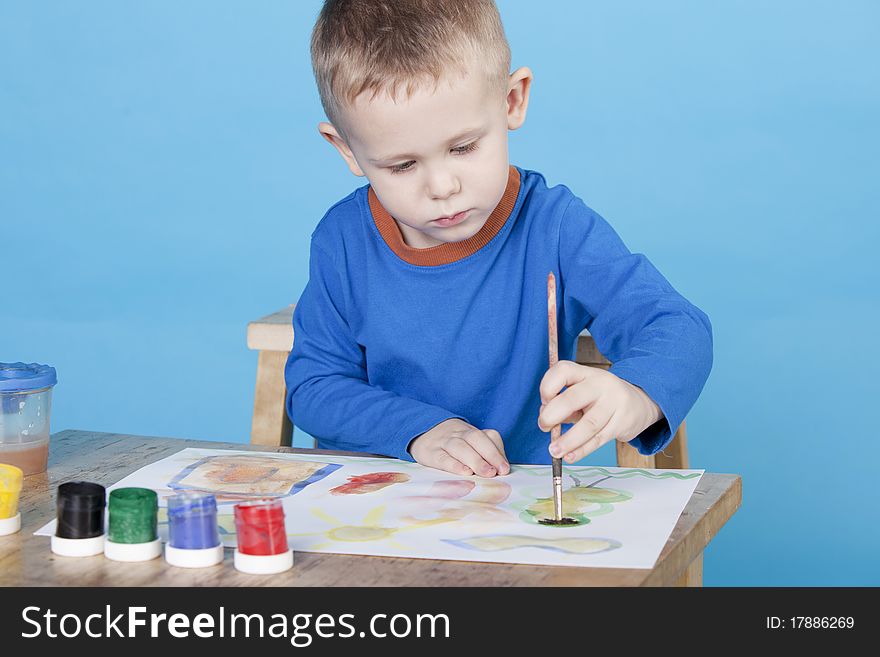 Beautiful thoughtful boy draws pictures on blue background