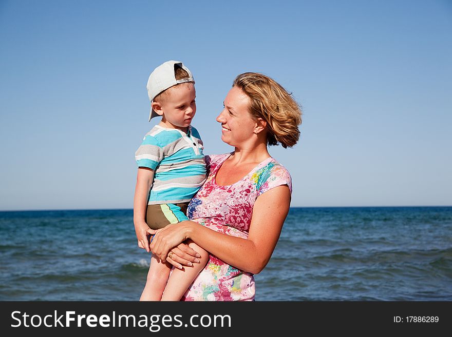 Beautiful mum holds the son on hands and looks at it on seacoast. Beautiful mum holds the son on hands and looks at it on seacoast