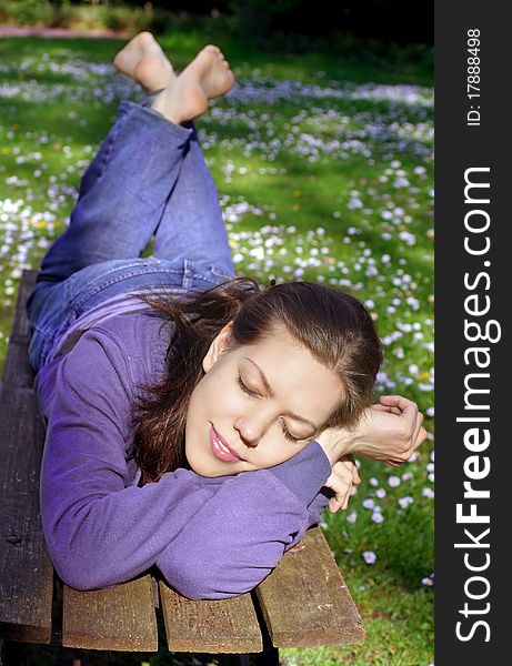 Young woman enjoying the sun, lying on a bench on a meadow, with closed eyes, head on arms. Young woman enjoying the sun, lying on a bench on a meadow, with closed eyes, head on arms