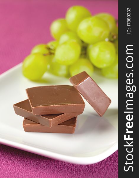 Chocolate pieces stacked on plate with grapes. Chocolate pieces stacked on plate with grapes