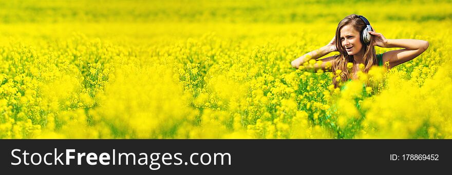 Young woman with headphones listening to music on oilseed flower field