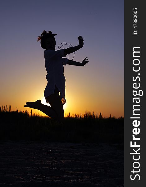 Silhouette of a young woman whearing a bandana and jumping at the sunset. Silhouette of a young woman whearing a bandana and jumping at the sunset