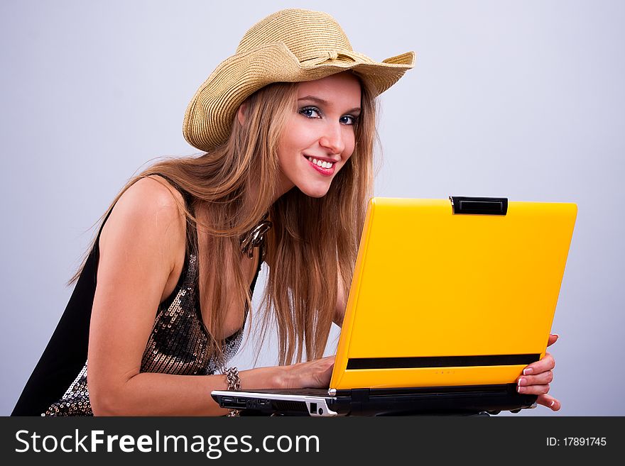 Attractive girl in a straw hat wth a yellow laptop
