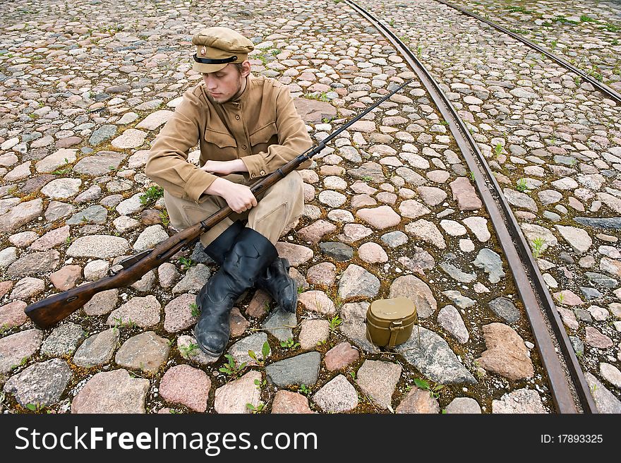 Soldier with gun and boiler in uniform of World War I, sit down and resting on the pavement. Costume accord the times of World War I. Photo made at cinema city Cinevilla in Latvia. Soldier with gun and boiler in uniform of World War I, sit down and resting on the pavement. Costume accord the times of World War I. Photo made at cinema city Cinevilla in Latvia.