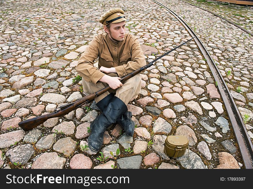 Soldier with gun and boiler in uniform of World War I, sit down and resting on the pavement. Costume accord the times of World War I. Photo made at cinema city Cinevilla in Latvia. Soldier with gun and boiler in uniform of World War I, sit down and resting on the pavement. Costume accord the times of World War I. Photo made at cinema city Cinevilla in Latvia.