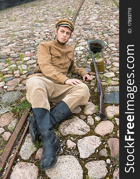 Soldier with gun and boiler in uniform of World War I, resting on the pavement. Costume accord the times of World War I. Photo made at cinema city Cinevilla in Latvia. Soldier with gun and boiler in uniform of World War I, resting on the pavement. Costume accord the times of World War I. Photo made at cinema city Cinevilla in Latvia.