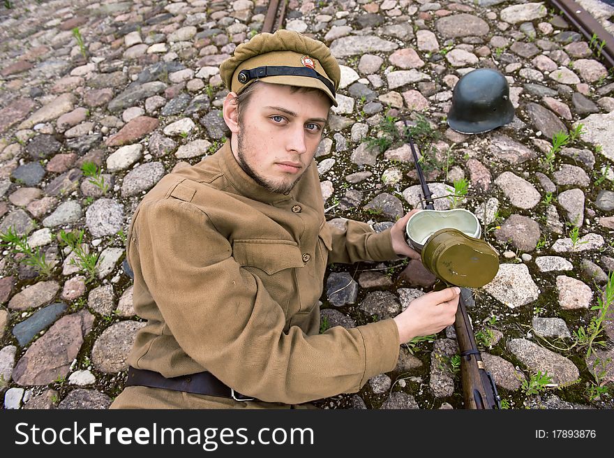 Soldier with gun and boiler in uniform of World War I, resting on the pavement. Costume accord the times of World War I. Photo made at cinema city Cinevilla in Latvia. Cockade on the hat do not contain trade mark. Soldier with gun and boiler in uniform of World War I, resting on the pavement. Costume accord the times of World War I. Photo made at cinema city Cinevilla in Latvia. Cockade on the hat do not contain trade mark.