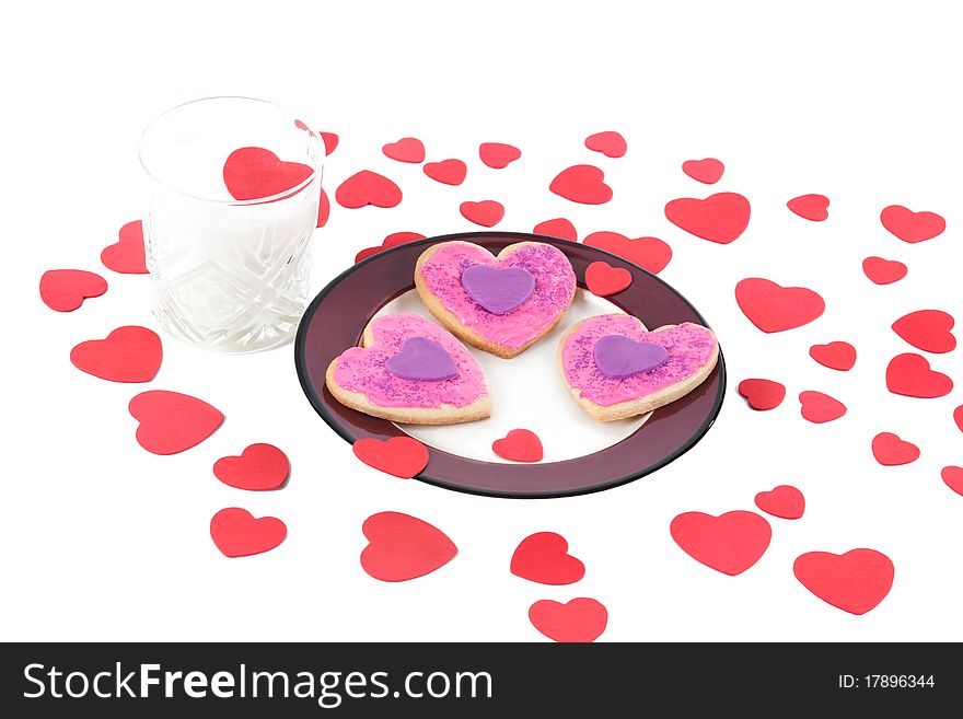 An angled closeup of a plate of homemade valentine cookies and a glass of milk with a valentine heart floating on top on a white isolated background. An angled closeup of a plate of homemade valentine cookies and a glass of milk with a valentine heart floating on top on a white isolated background.