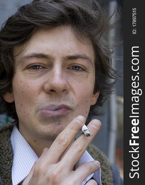 A young man smokes a cigarette. He's looking directly at the camera. He's rebelious and confident. A young man smokes a cigarette. He's looking directly at the camera. He's rebelious and confident.