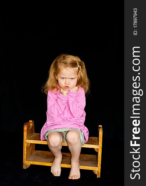 A cute girl sitting on a chair/stool. She has a very unique facial expression. She is pouting and thinking. A cute girl sitting on a chair/stool. She has a very unique facial expression. She is pouting and thinking.