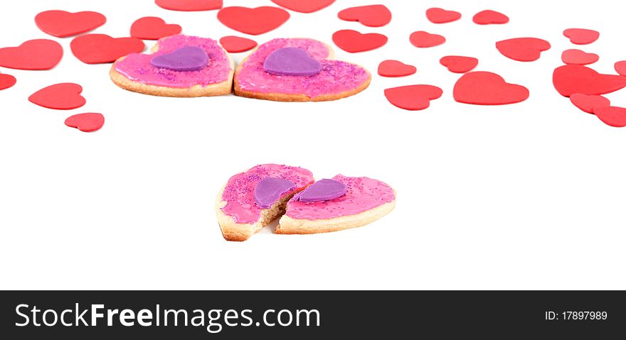A front angled macro view of a couple a broken valentine cookie with couple of cookies in the back within a sea of valentines on an isolated white background. A front angled macro view of a couple a broken valentine cookie with couple of cookies in the back within a sea of valentines on an isolated white background.