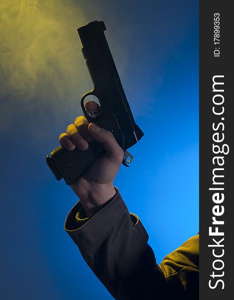 Private detective holding a gun, shooted in studio on a blue background with yellow light and smoke. Private detective holding a gun, shooted in studio on a blue background with yellow light and smoke