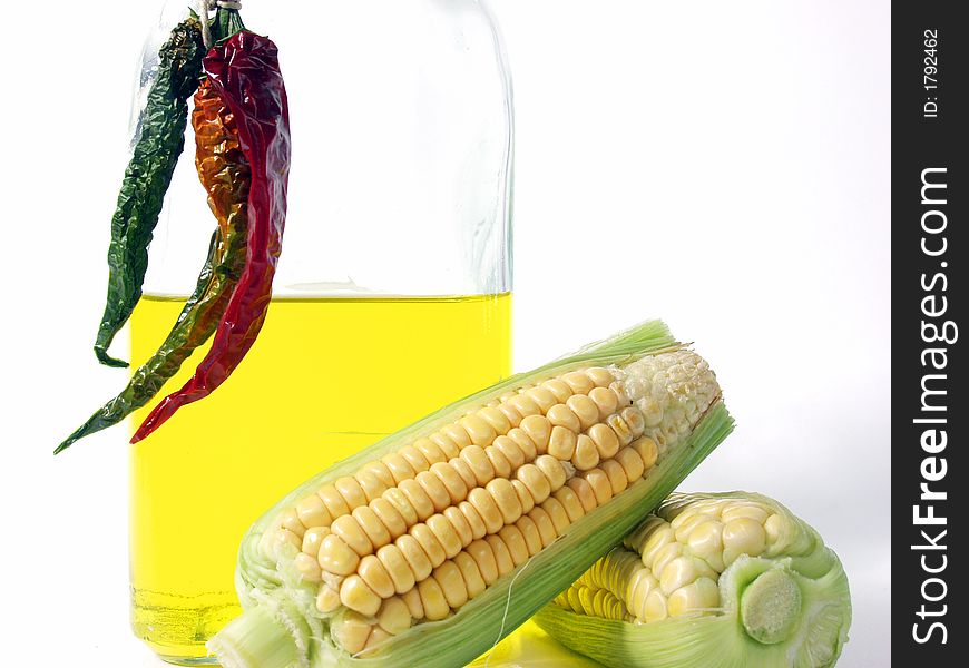 Bottle of yellow oil and fresh corn on the cob with pepper