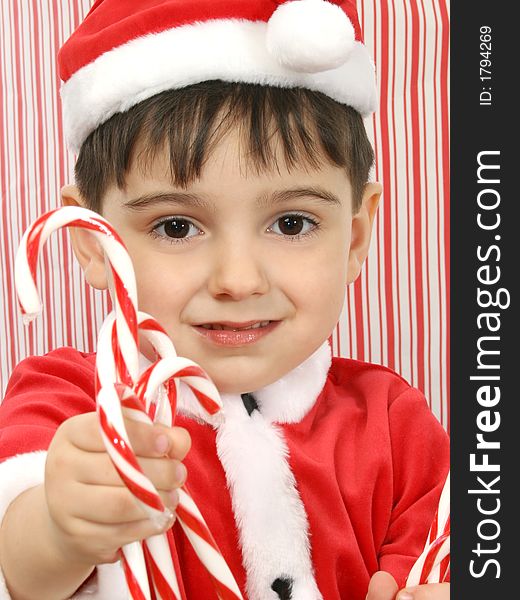 Boy in santa suit offering candy canes.