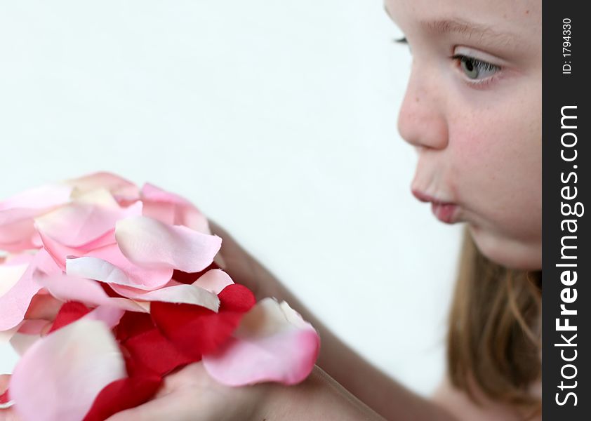 Young girl blowing pink, red, white rose petals held in hands. Young girl blowing pink, red, white rose petals held in hands