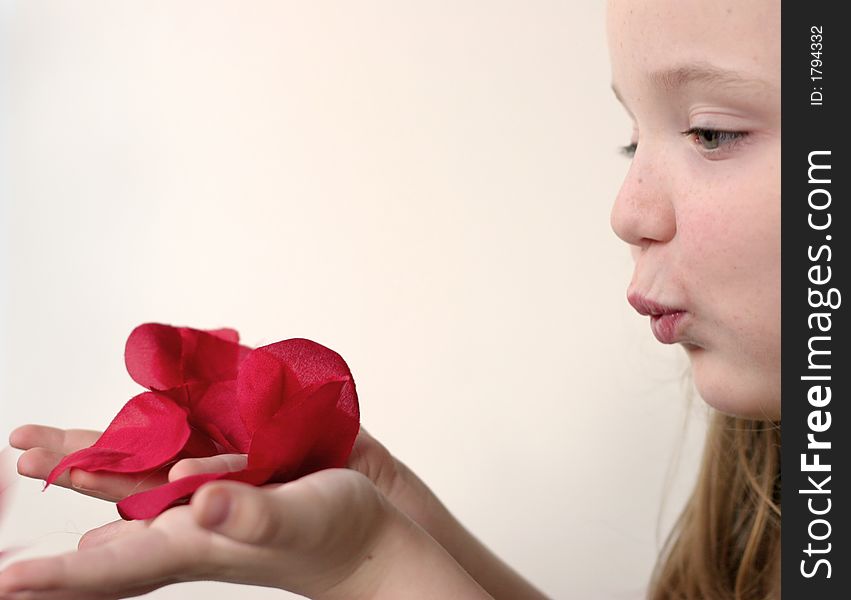 Young girl blowing pink, red, white rose petals held in hands over a slightly pink background. Young girl blowing pink, red, white rose petals held in hands over a slightly pink background