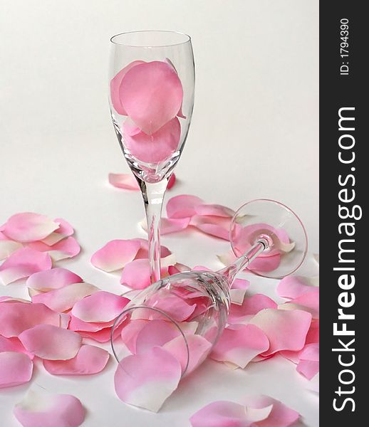 Pink and white rose petals surrounding two wine glasses. Pink and white rose petals surrounding two wine glasses