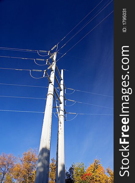 Power lines towers over autumn treetops - blue sky with wispy clouds to right. Power lines towers over autumn treetops - blue sky with wispy clouds to right
