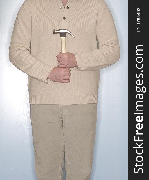 Man dressed in off-white clothing holds a hammer in front of his body while he stands in front of a blue background. Man dressed in off-white clothing holds a hammer in front of his body while he stands in front of a blue background