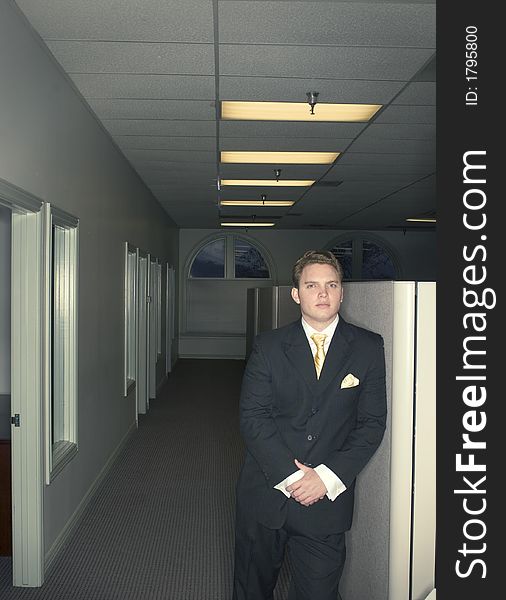 Businessman standing against a wall in the office with his hands folded in front of him