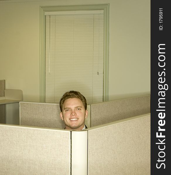 Businessman smiles and shows his head above the office cubicles