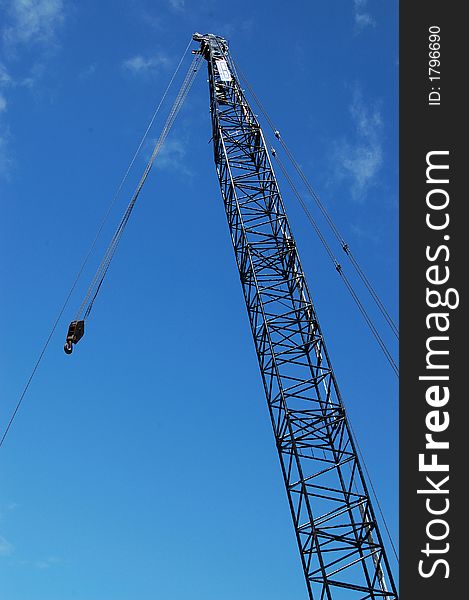 Silhouette of crane and hook against blue sky and some cloud